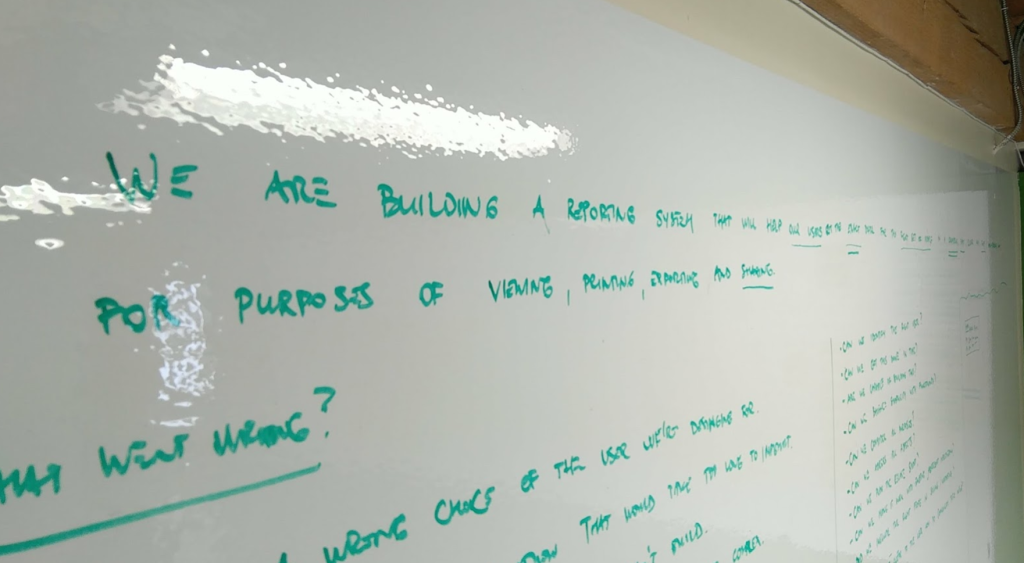 A whiteboard with handwriting. Only the start of the sentence is legible: "We are building a reporting system..."